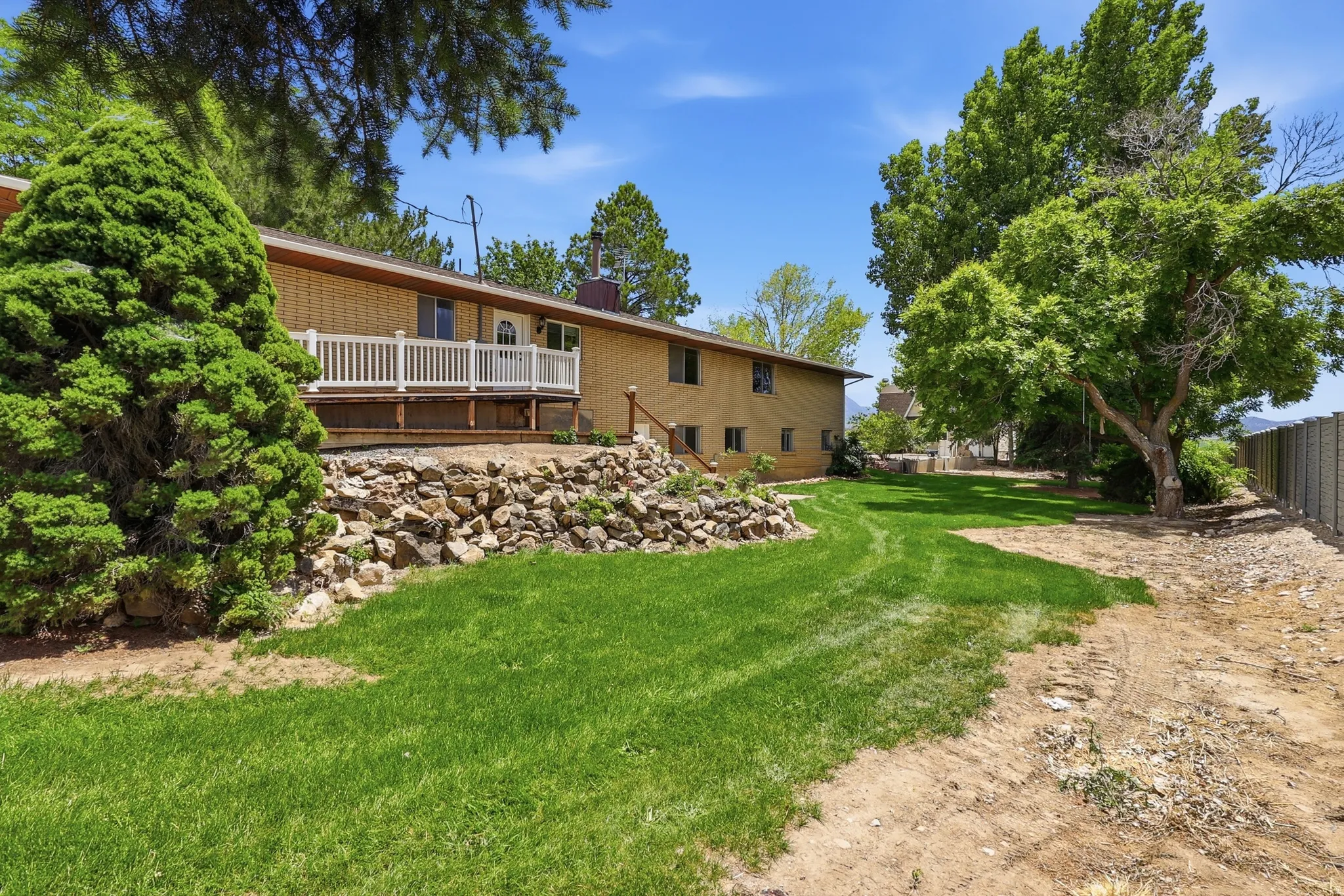 Expansive backyard featuring a manicured lawn, established trees, and a brick exterior home with a white railed deck