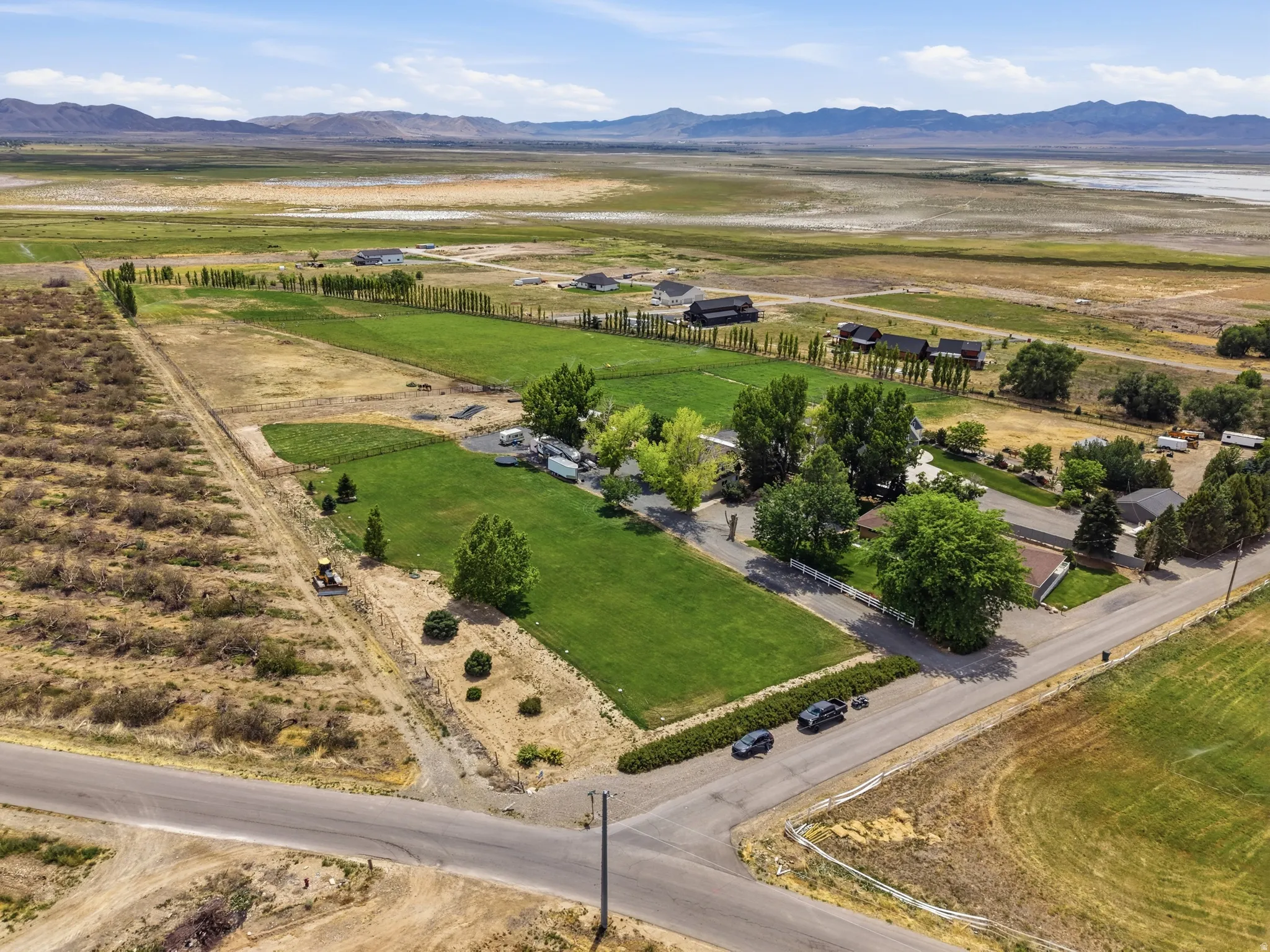 Expansive rural property featuring a large green lawn, mature trees, and a paved road frontage