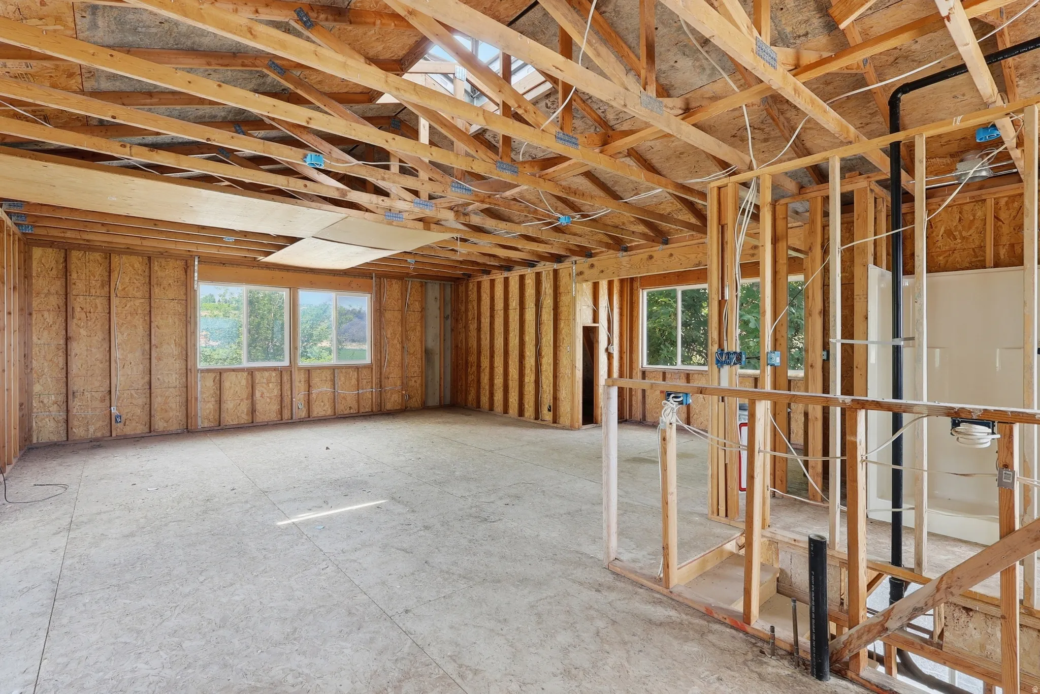 Unfinished interior space featuring exposed wood framing, ceiling trusses, and plywood subflooring