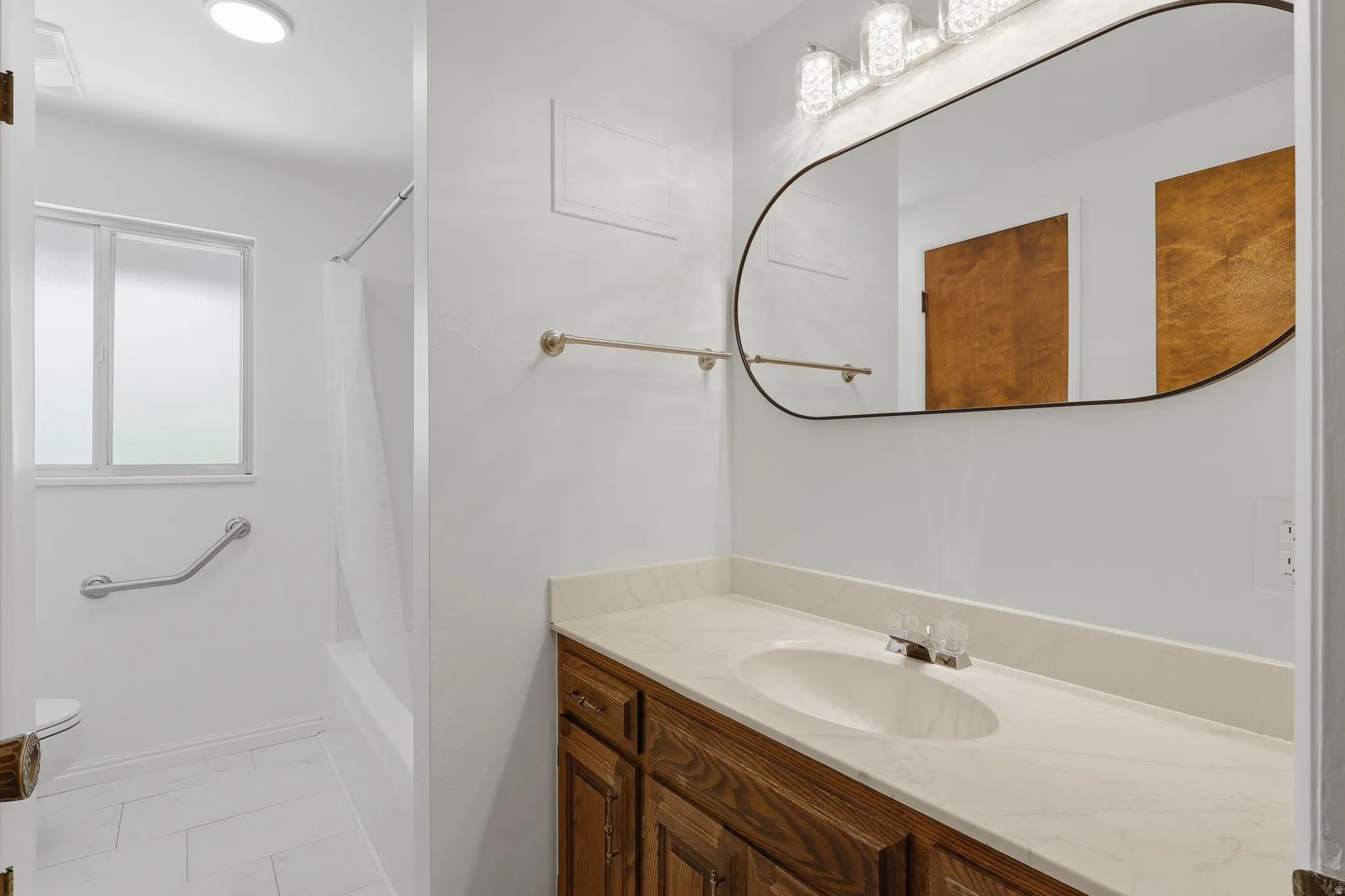 Bathroom featuring a wood vanity with an integrated sink, a rectangular mirror, and a tub/shower combination with a privacy window
