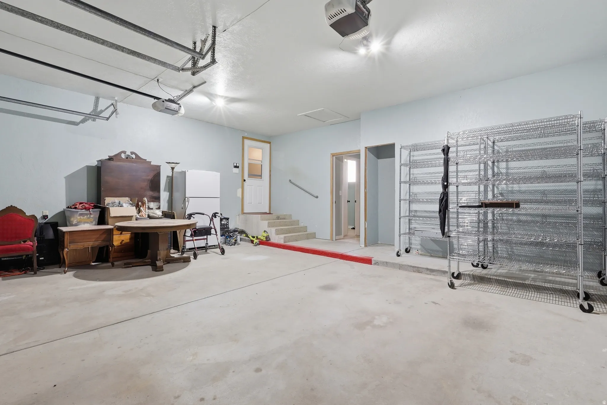Spacious garage featuring a concrete floor, light blue walls, overhead lighting, and an automatic garage door opener system