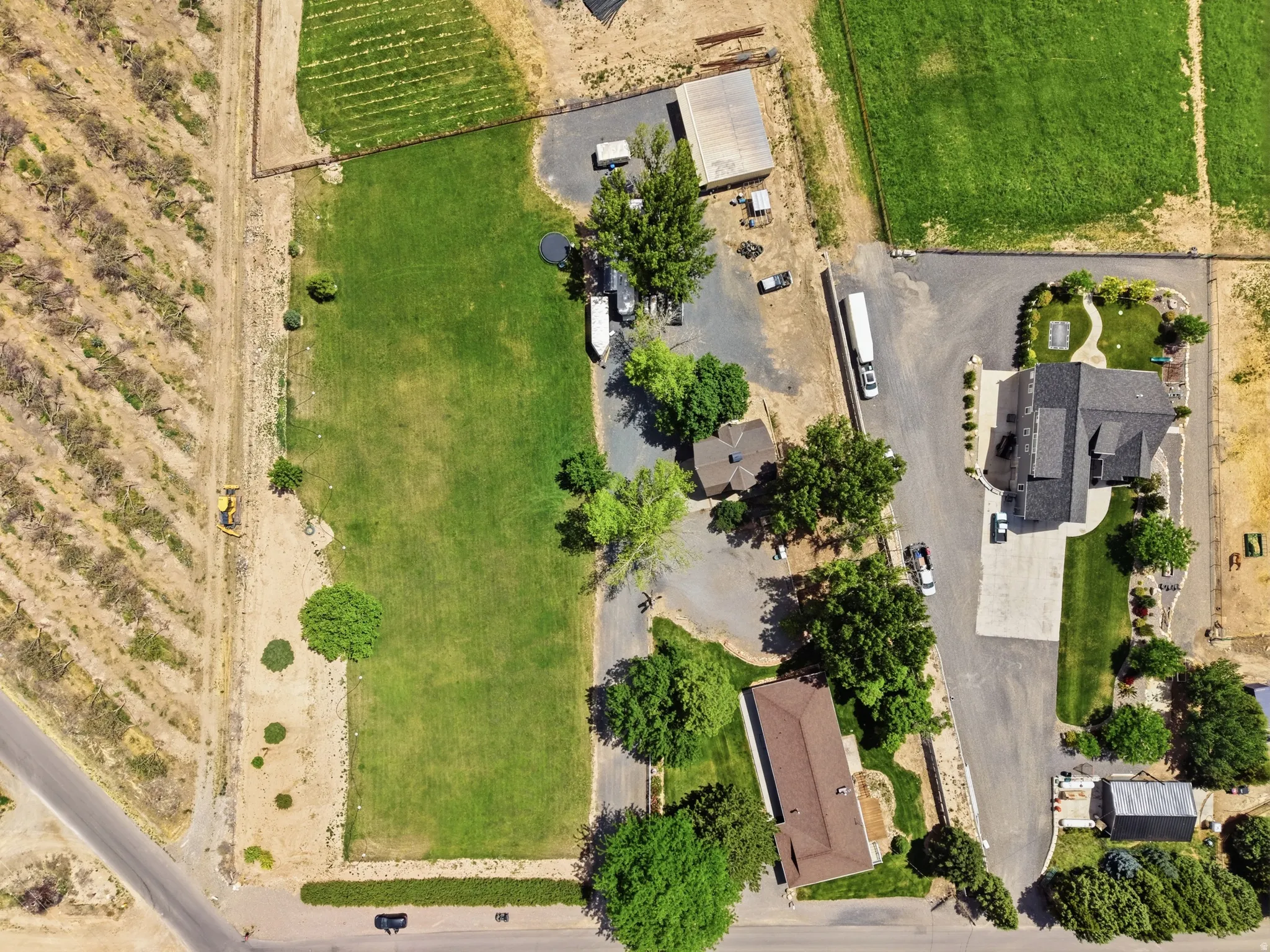Expansive property featuring multiple structures, mature trees, manicured lawns, paved driveways, and an adjacent agricultural field