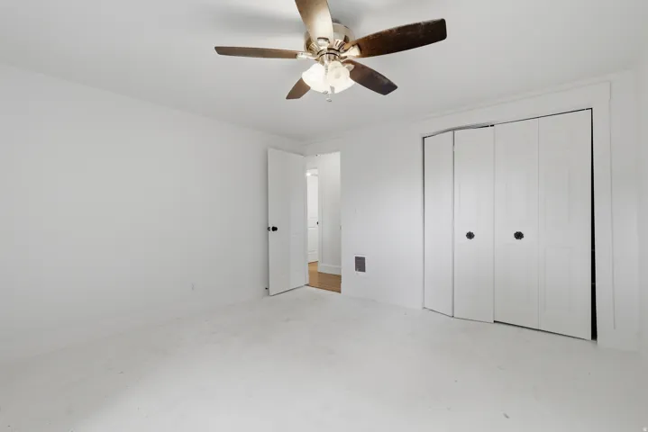 Room featuring white walls and ceiling, a ceiling fan with light fixture, carpeted flooring, a panel door, and bi-fold closet doors
