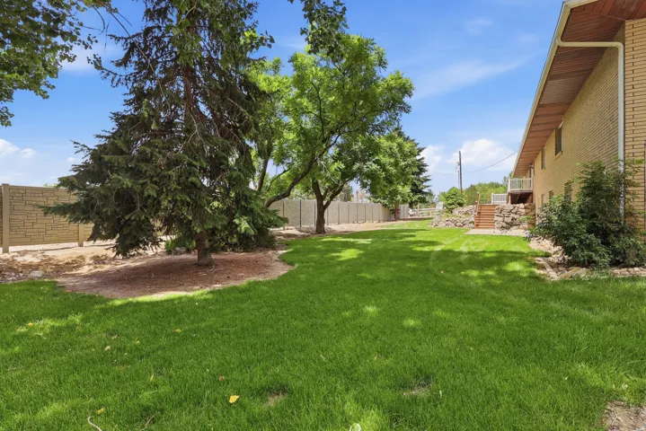 Expansive lawn area featuring mature trees, a decorative stone-patterned fence, and a brick exterior building with a wood-soffit overhang