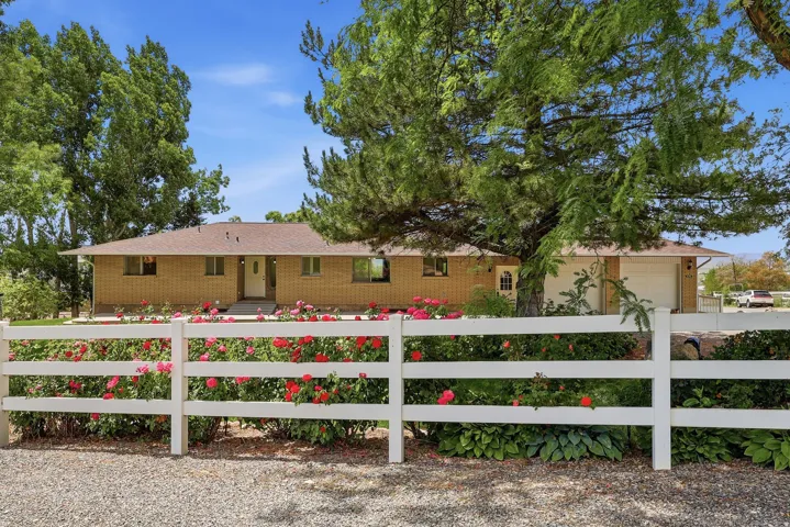 Brick exterior residence with a white picket fence, mature trees, a gravel driveway, and an attached garage