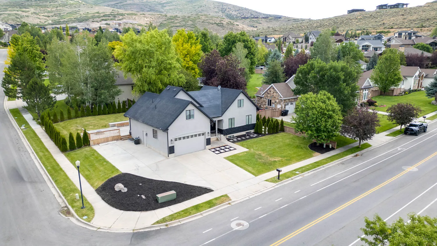 Contemporary-style residence featuring a two-car garage, manicured front lawn, and mature perimeter trees
