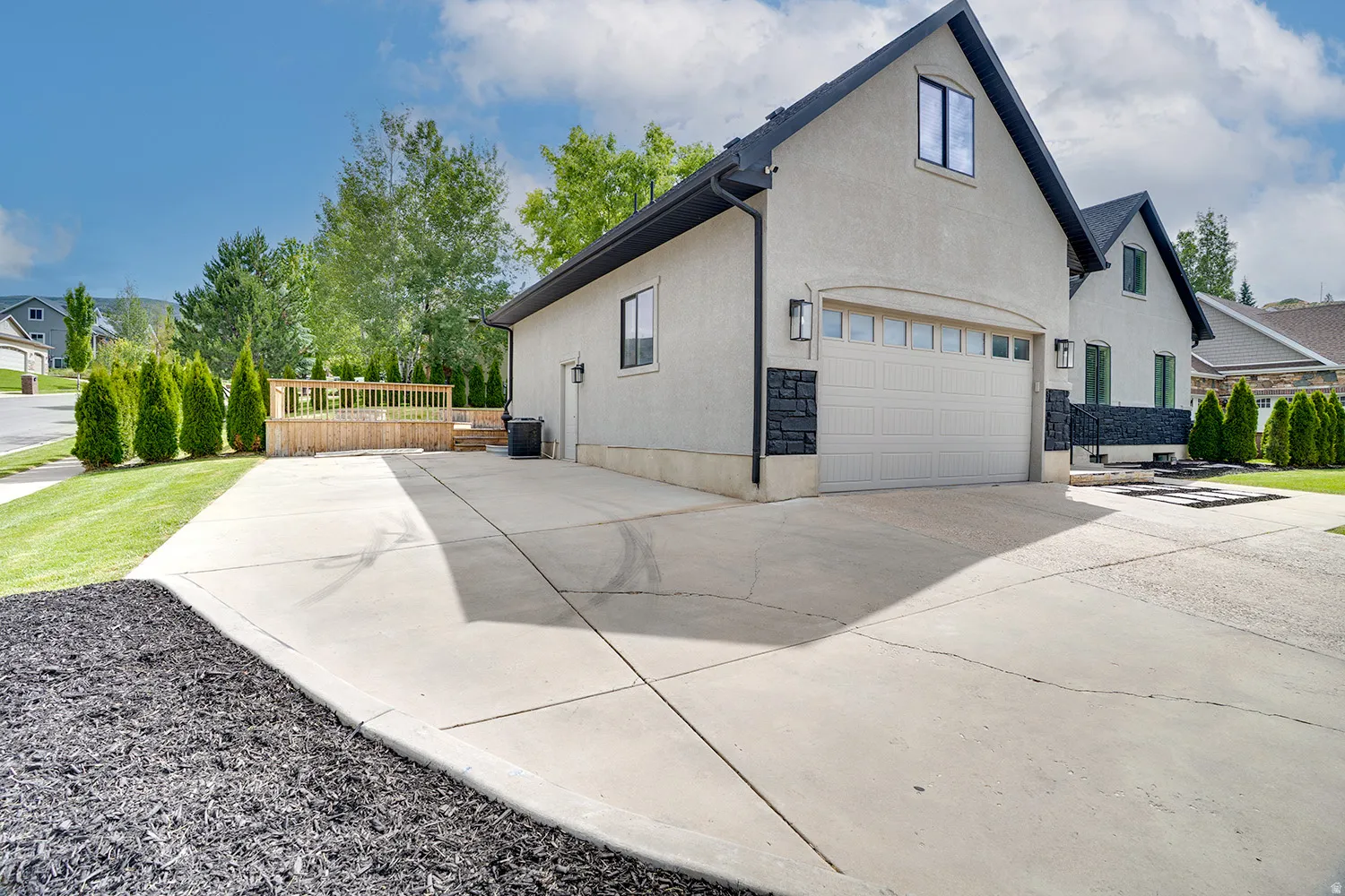 Stucco exterior with a pitched roof, attached garage, extended concrete driveway, and a wood deck with railings
