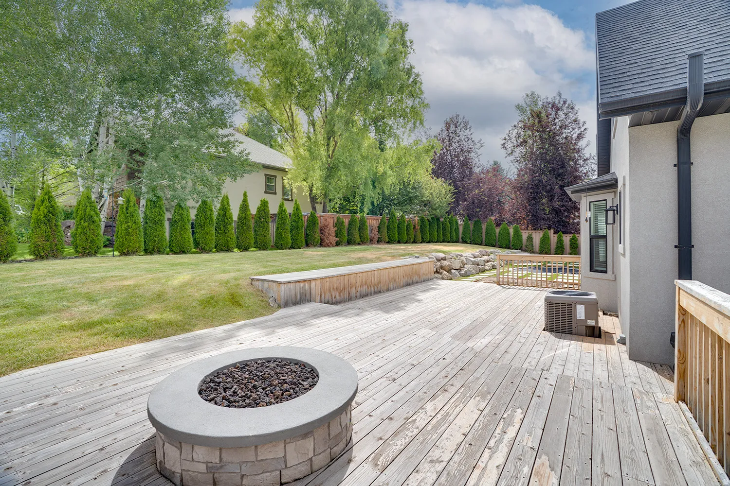 Expansive wood deck featuring a built-in fire pit with stone surround and a raised wood planter box