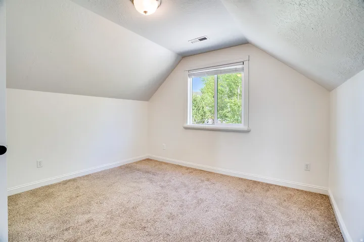 Carpeted room featuring an angled ceiling and a single window with white trim