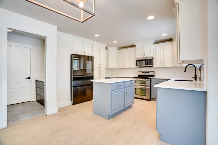 Modern kitchen featuring light wood-finish flooring, white upper cabinetry, and contrasting blue-gray lower cabinetry