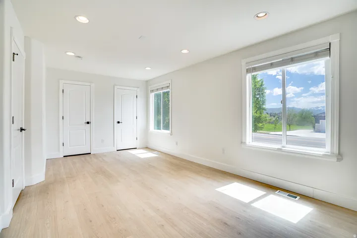 Bright room featuring wood-finish flooring, two white panel doors with black hardware, and recessed lighting