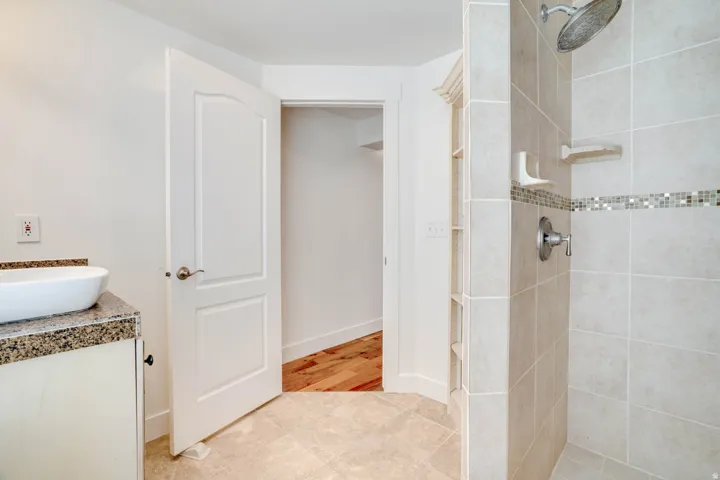 Bathroom featuring a vessel sink on a granite-look countertop vanity, tiled flooring, a walk-in shower with rain head and mosaic accent tile, and built-in shelving