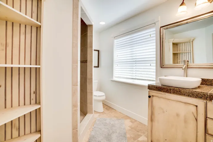 Bathroom featuring a stone tile shower, light wood vanity with a vessel sink, and a window with horizontal blinds