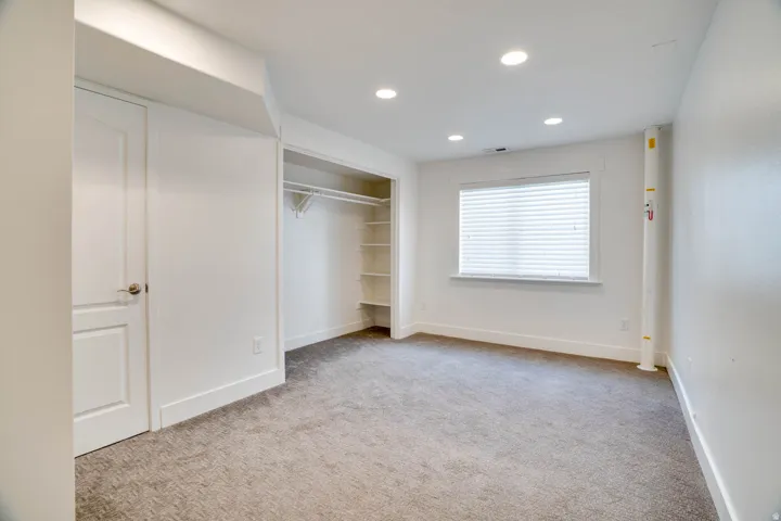 Carpeted room featuring a window with horizontal blinds, recessed lighting, a white two-panel door, and an open closet with shelving and hanging rods