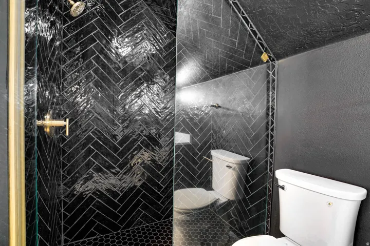 Walk-in shower featuring black herringbone tile, a gold-finish shower head, and gold-finish fixtures