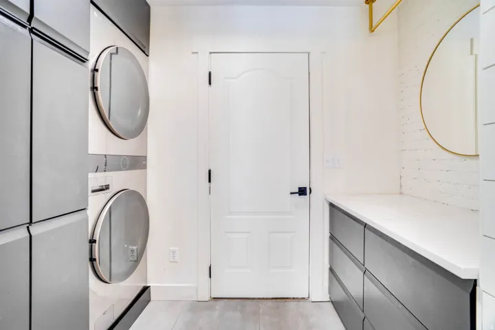 Dedicated laundry area featuring stacked front-load appliances and light wood-finish flooring