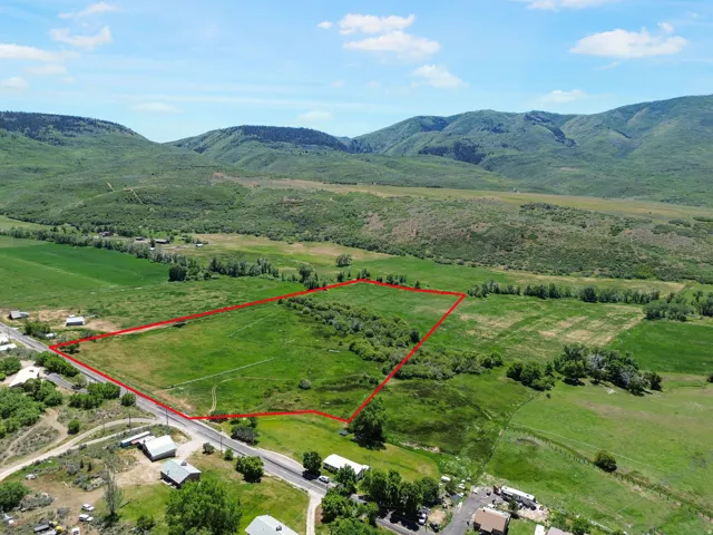 Expansive green land parcel featuring clear boundaries, a mountainous backdrop, and frontage along a paved road