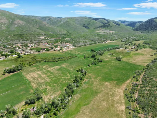 Expansive green fields within a valley setting, bordered by verdant, tree-covered hills