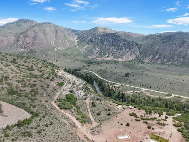 Expansive mountain landscape featuring a river, road, and varied terrain including natural vegetation and cleared areas