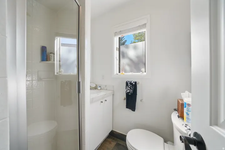 Contemporary bathroom featuring a glass-enclosed shower with white subway tile, a vanity with a stone-finish countertop, and dark-finish flooring