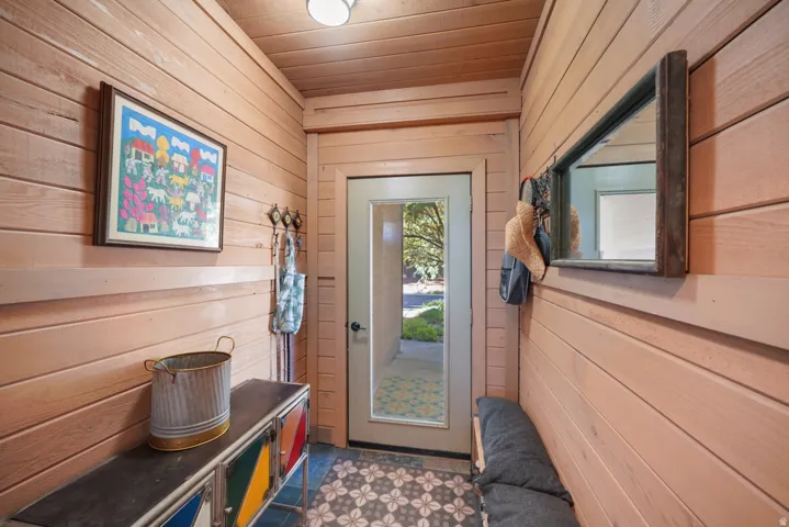 Entryway featuring horizontal wood paneling, a recessed light fixture, a glass-paneled door, and patterned floor tiling