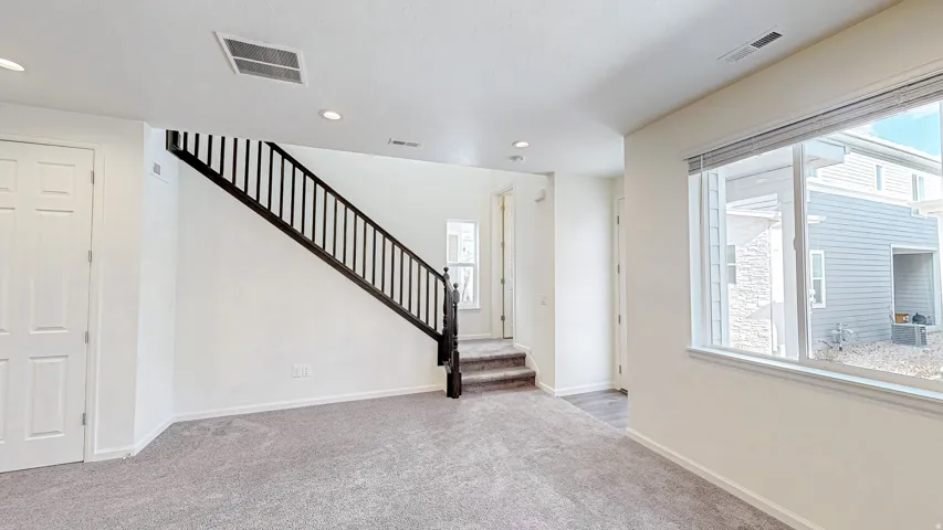 Carpeted living space featuring a dark wood staircase with spindle railing, recessed lighting, and a large window with blinds