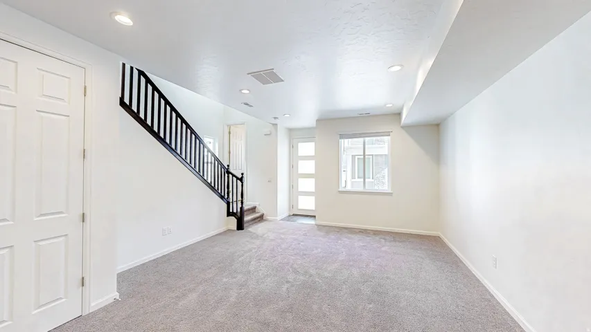 Open-concept area featuring light gray carpeting, recessed lighting, and a contemporary staircase with black railings
