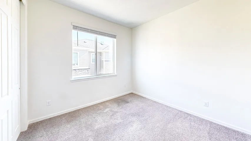 Carpeted room featuring a white-framed window, white walls, and a bi-fold closet door
