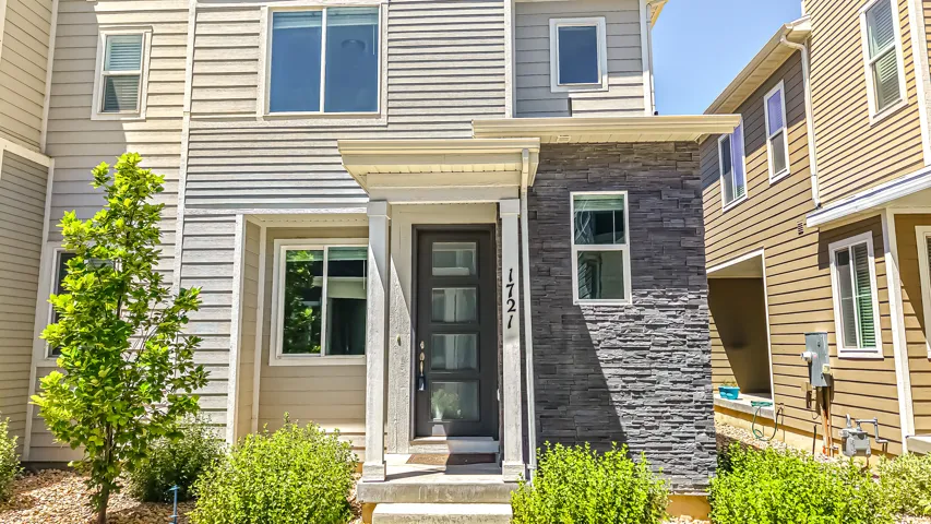 Modern townhouse exterior featuring a covered entry, stacked stone accents, horizontal siding, multiple windows, and manicured landscaping