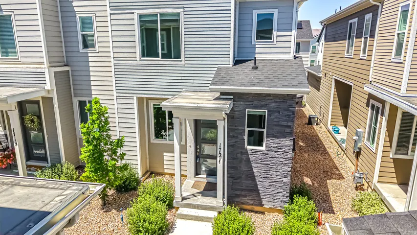 Contemporary multi-story exterior featuring light gray horizontal siding, a covered entry with stone facade accents, a dark entry door with frosted glass panels, and landscaping with gravel and shrubs