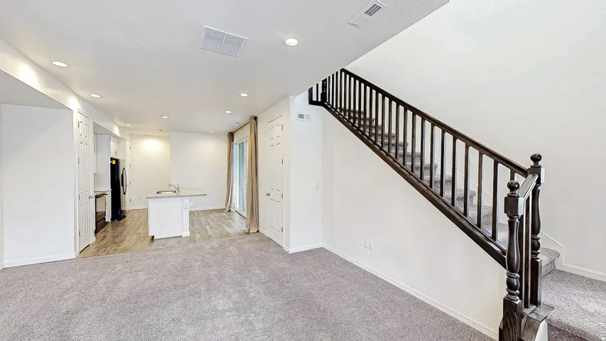 Open-concept living space featuring light gray carpet, recessed lighting, and a dark wood staircase with carpeted treads