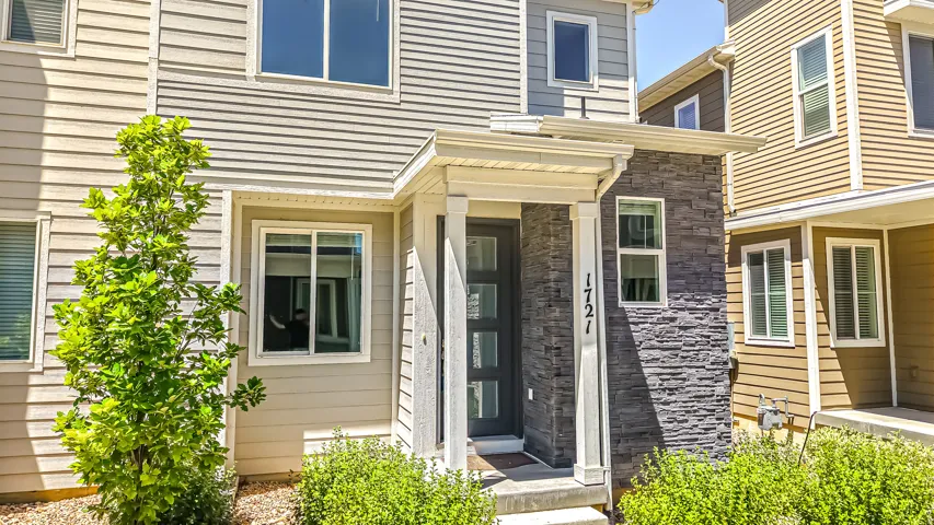 Modern townhome exterior featuring layered siding, a stone facade accent, and an integrated porch