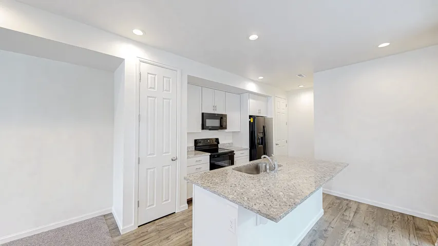 Kitchen featuring an island with an undermount sink, granite countertop, recessed lighting, white cabinetry, and wood-finish flooring