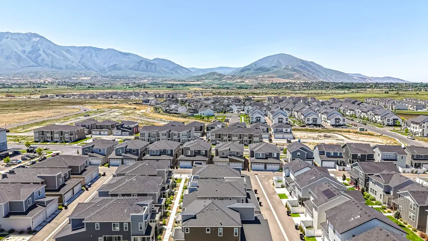 Expansive residential development featuring contemporary homes with dark shingle roofs, structured street layouts, and mountain backdrop