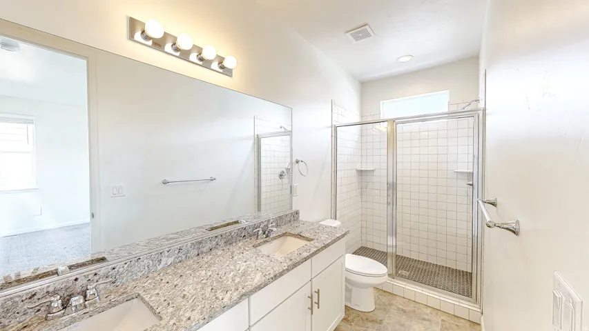 Bathroom featuring a double vanity with stone countertops, a large frameless mirror, and a walk-in shower with white subway tile and a glass enclosure
