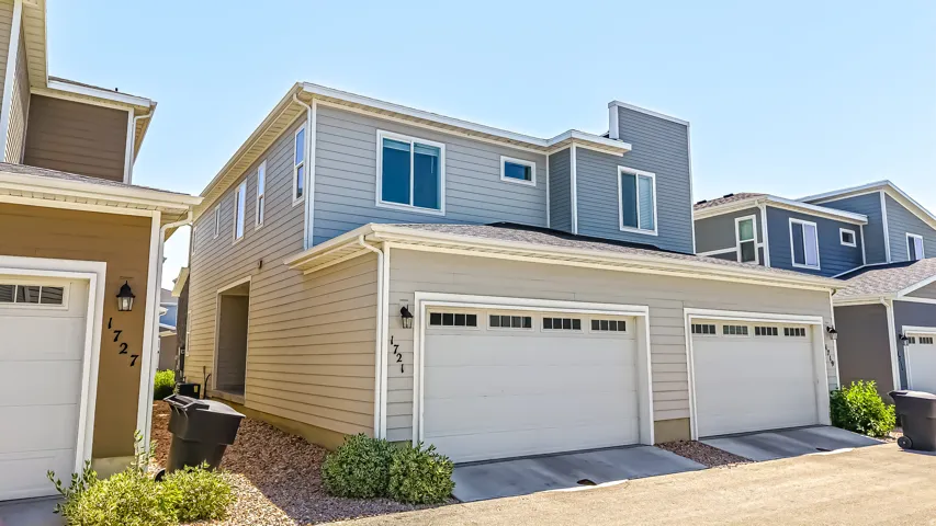 Contemporary townhouse exterior featuring a two-car garage, light gray siding, and white trim accents