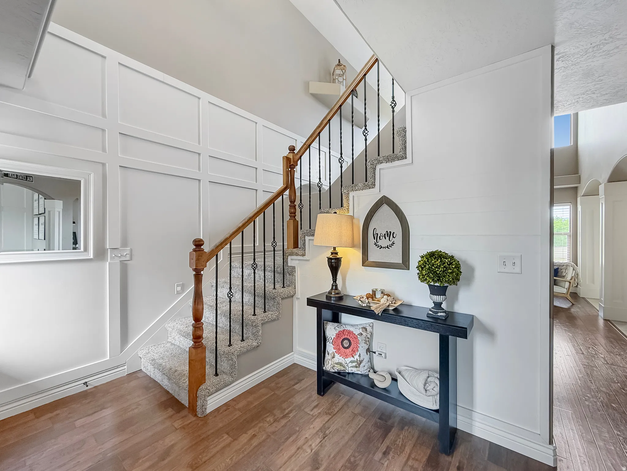 Foyer featuring wood-finish flooring, wainscoting, and a staircase with wood newel posts, a wood handrail, and black iron balusters