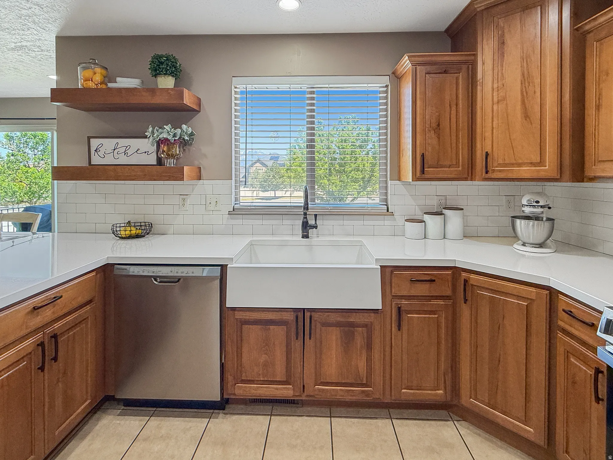Kitchen featuring wood cabinetry, white countertops, subway tile backsplash, a farmhouse sink, and a stainless steel dishwasher