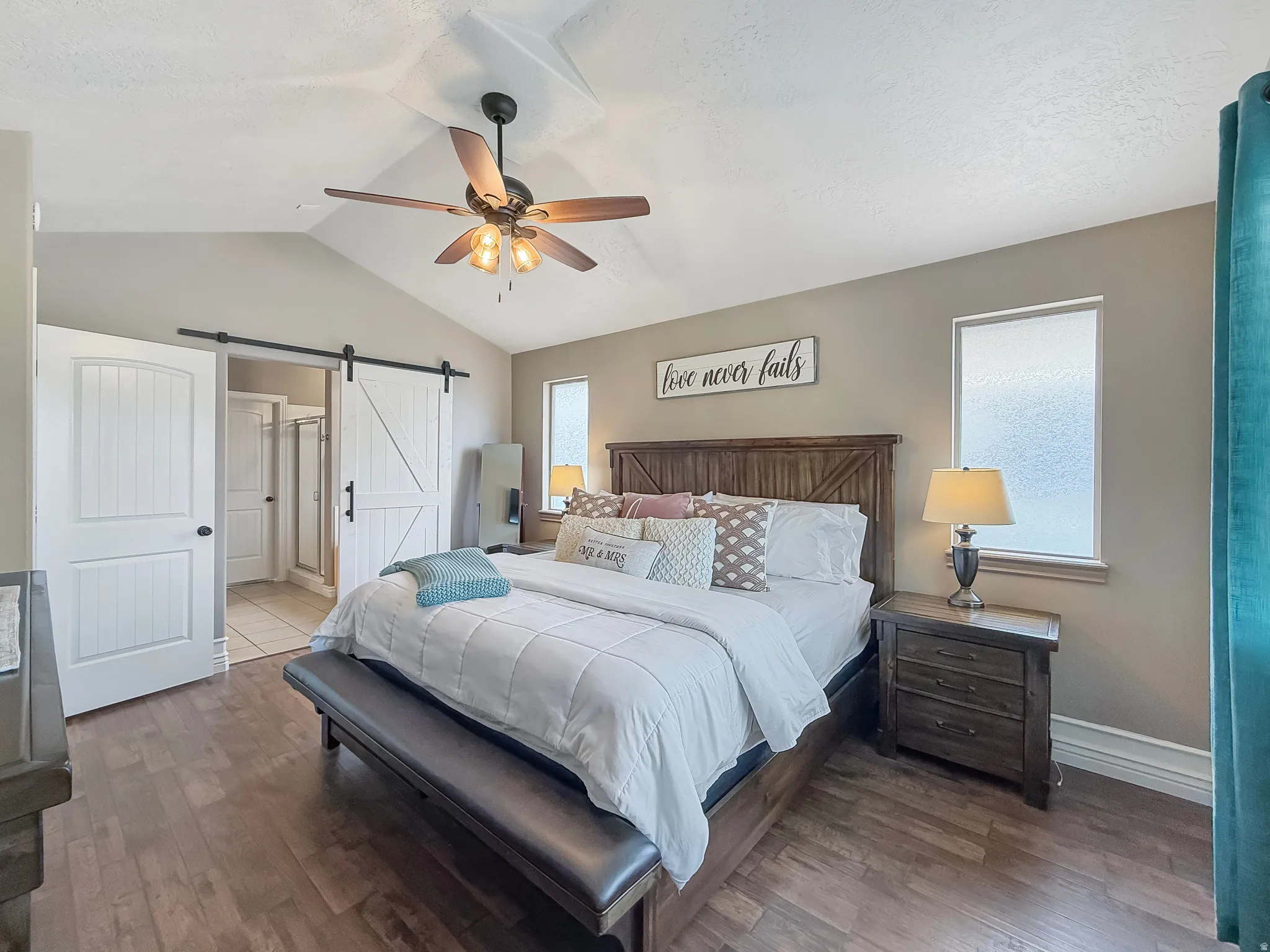 Vaulted ceilings with a ceiling fan light fixture, wood-finish flooring, two windows with privacy glass, and a barn door entry to an adjoining space with tile flooring