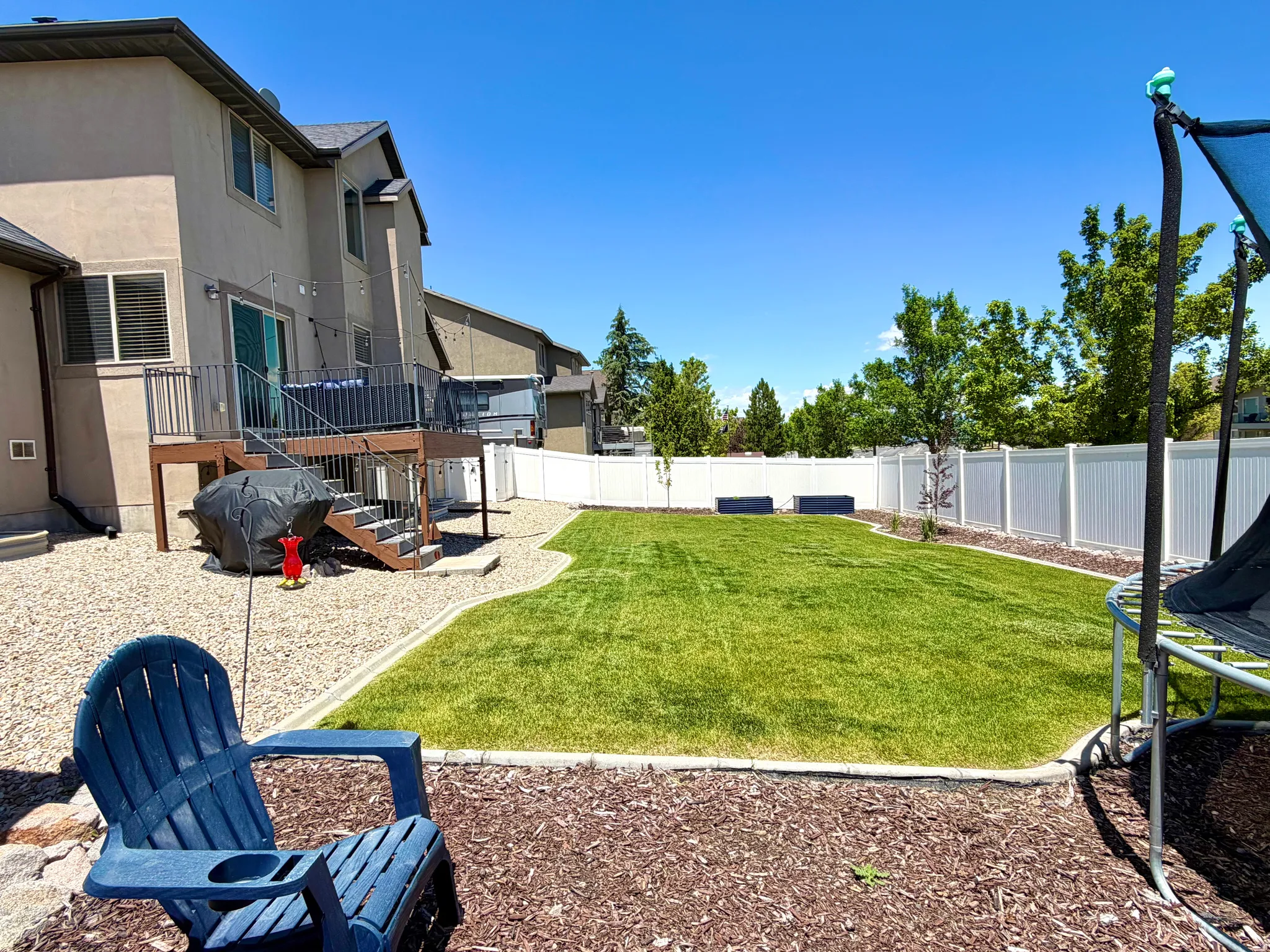 Expansive backyard featuring a manicured lawn, white privacy fencing, and mature trees