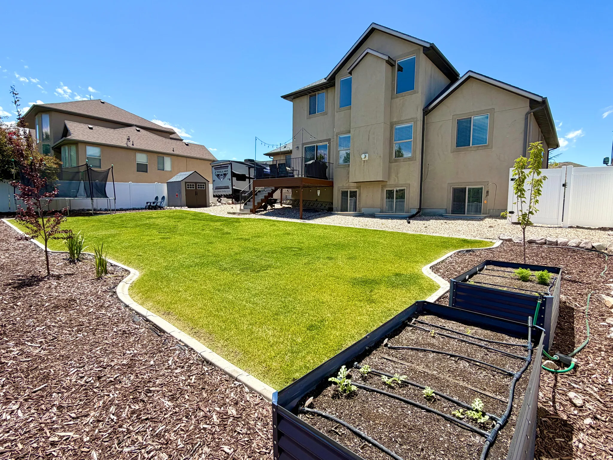 Expansive backyard featuring a manicured lawn, established landscaping beds with wood chips, and two elevated garden planters with irrigation