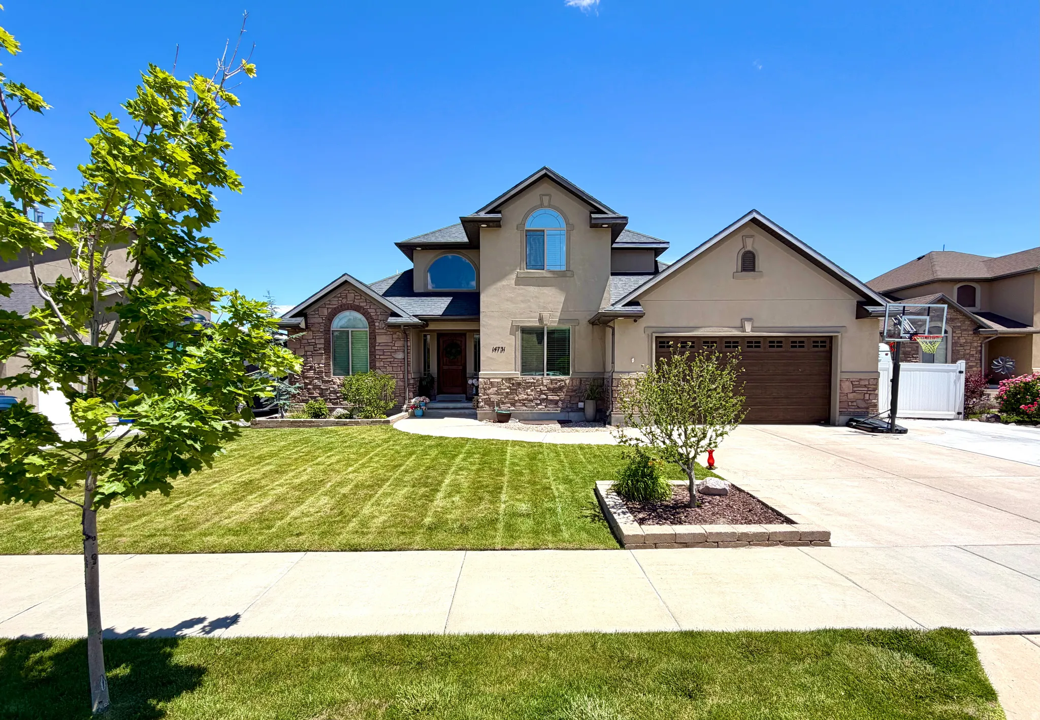 Stucco and stone exterior featuring an arched window, a two-car garage with a wood-finish door, a concrete driveway, and a front lawn with planted landscaping