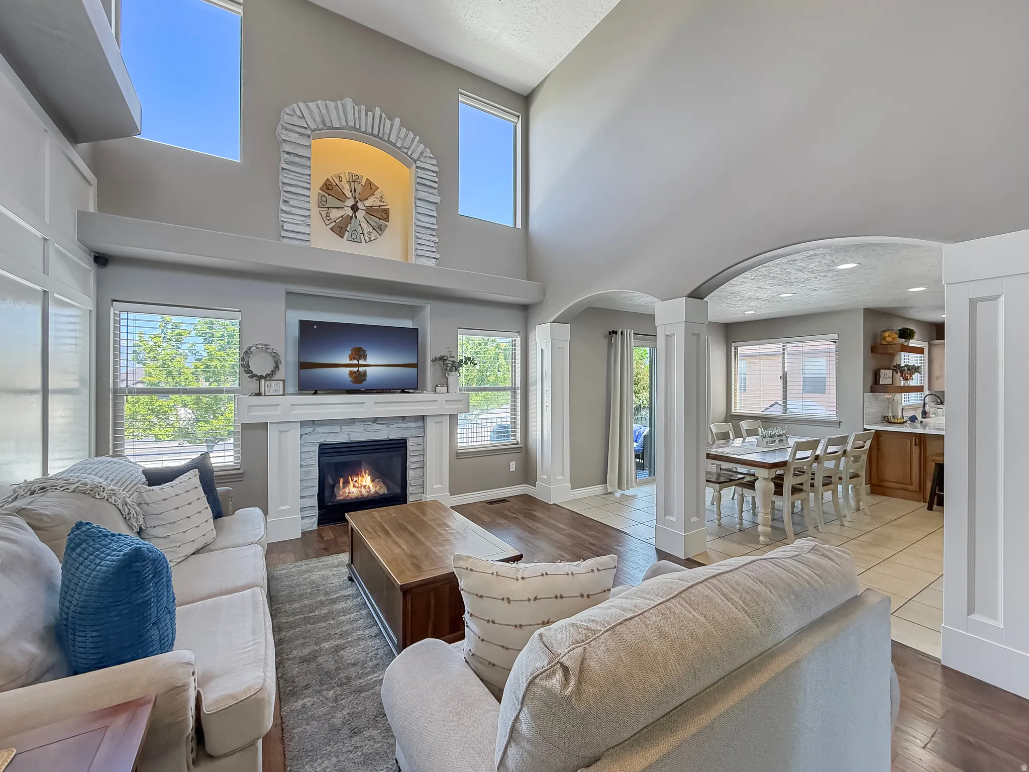 Vaulted ceilings enhance this living area featuring a stone-faced fireplace with a white mantel, wood-finish flooring, and ample natural light from multiple windows