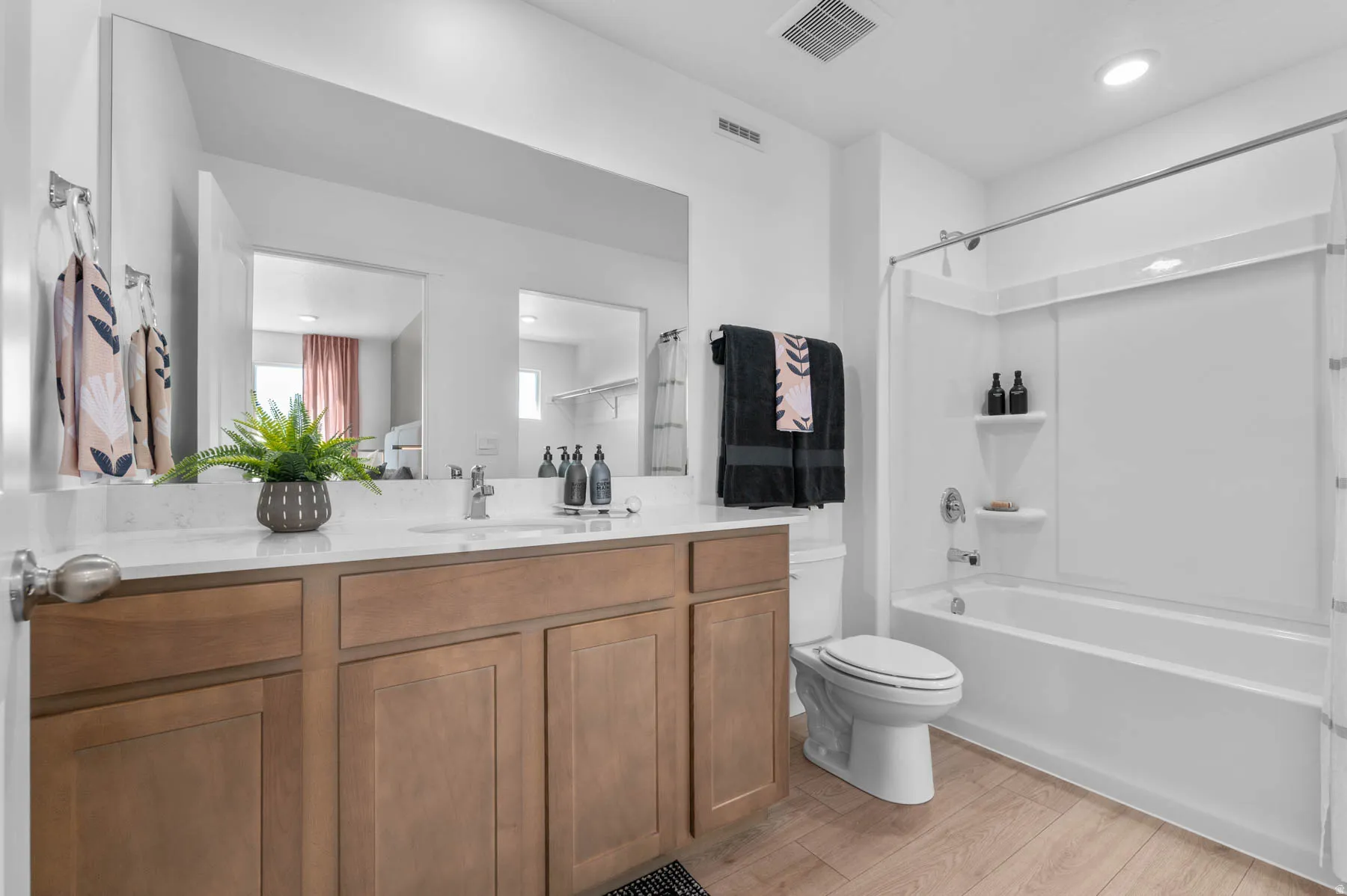 Bathroom featuring a wood-finish vanity with a light-toned countertop, a large wall-mounted mirror, white toilet, and a white bathtub with an integrated shower