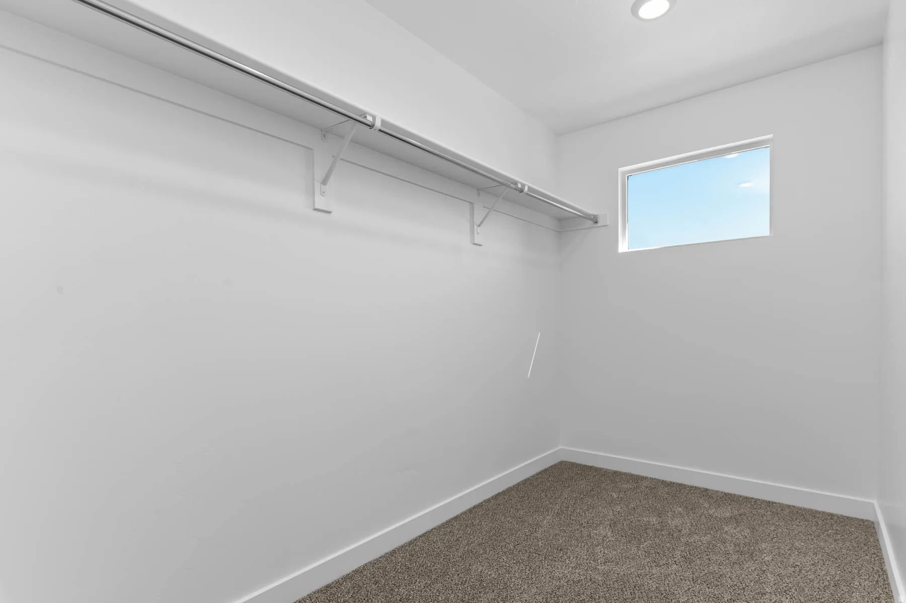 Recessed lighting illuminates this room featuring wall-to-wall carpeting, a horizontal window, and a built-in clothing rod with shelving