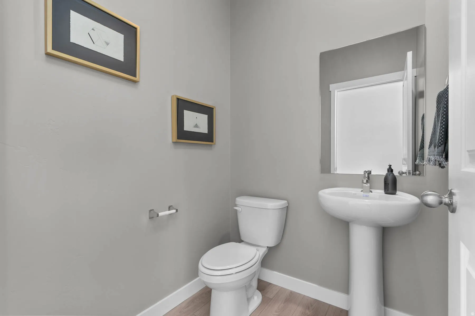 Pedestal sink with chrome faucet, toilet, and wood-finish flooring