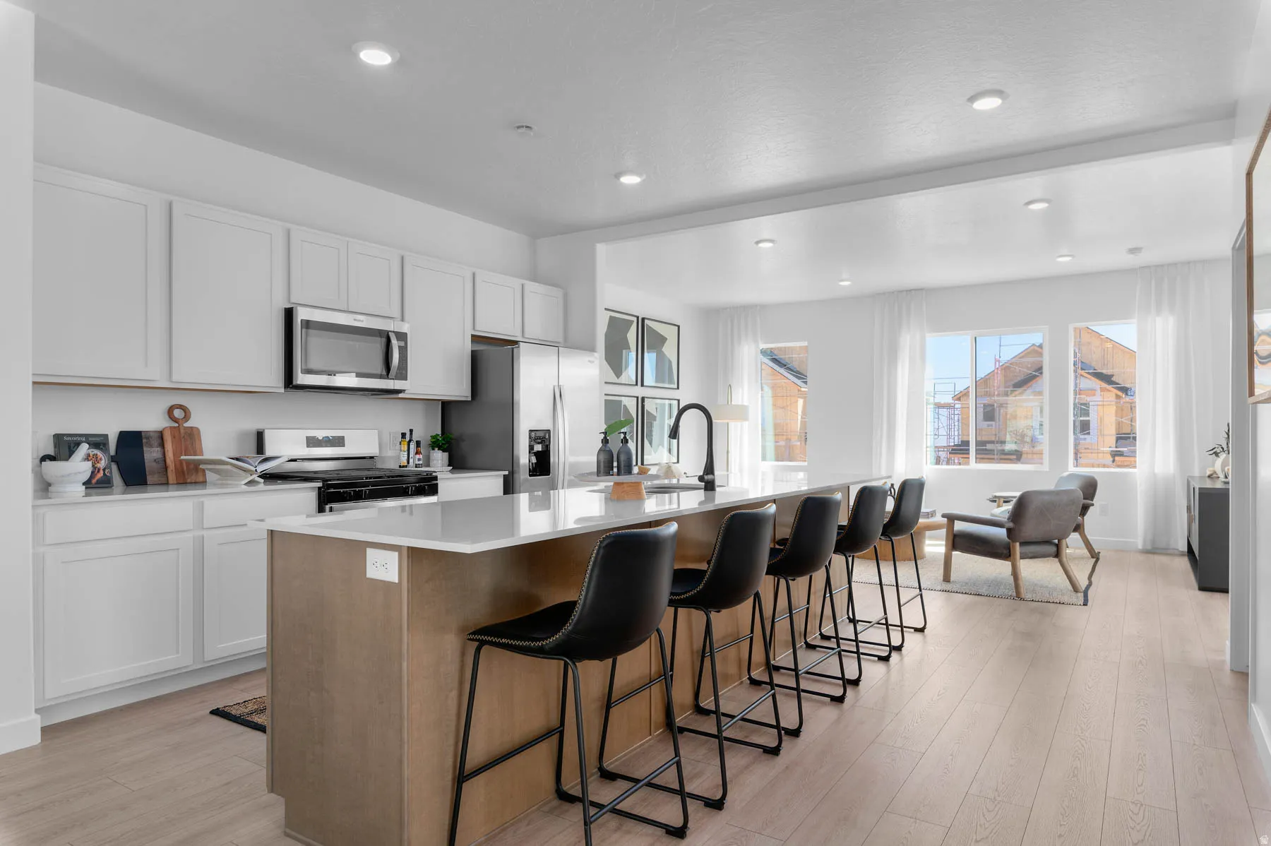Open-concept kitchen featuring white cabinetry, stainless steel appliances, a light-toned island with integrated seating, a black faucet, and wood-finish flooring