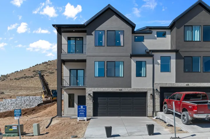 Contemporary multi-story exterior featuring a two-tone facade, private balconies with black railings, a two-car garage with a modern door, and a concrete driveway