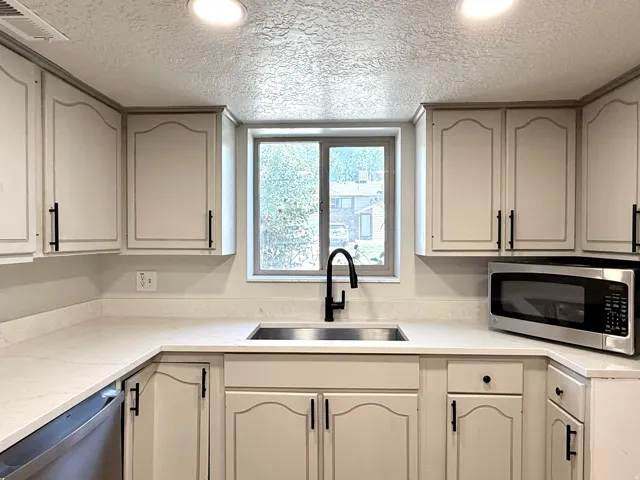 Kitchen featuring ample cabinetry, light-toned countertops, a stainless steel sink, and a modern black faucet