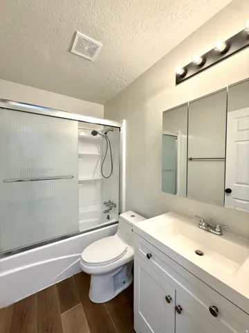 Full bathroom featuring a white vanity with integrated sink, wood-finish flooring, and a tub-shower combination with frosted sliding glass doors